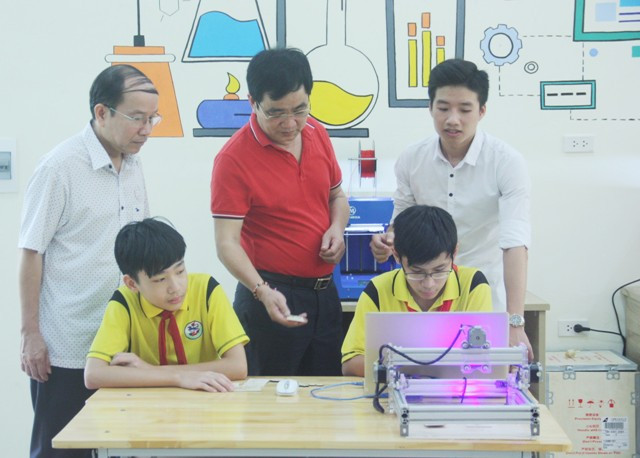 Thầy Đoàn Công Thạo (áo đỏ) - Hiệu trưởng trường THCS Giảng Võ đang cầm sản phẩm do chính học sinh của mình làm ra từ máy khắc CNC