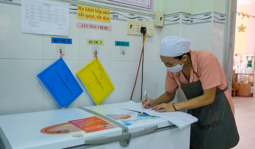 Nhân viên cung cấp thực phẩm trường học tiến hành lưu mẫu thức ăn và ghi vào sổ theo dõi. Ảnh minh họa