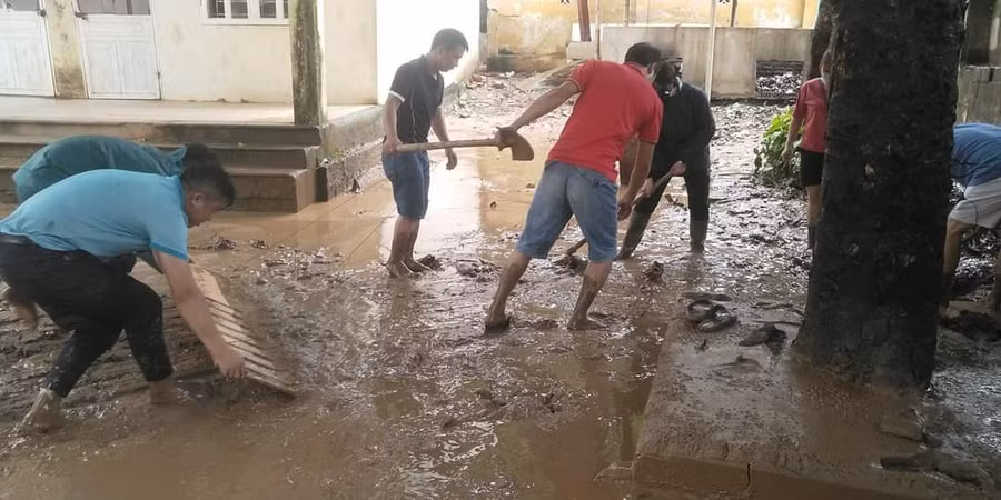 Giáo viên và phụ huynh dọn dẹp khuôn viên trường học sau khi bị nước lũ và bùn đất tràn vào.