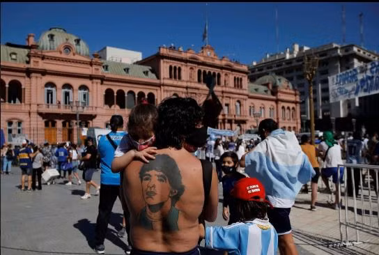 Một người đàn ông với hình xăm Maradona trên lưng cố dõi ánh mắt theo đoàn xe tang.