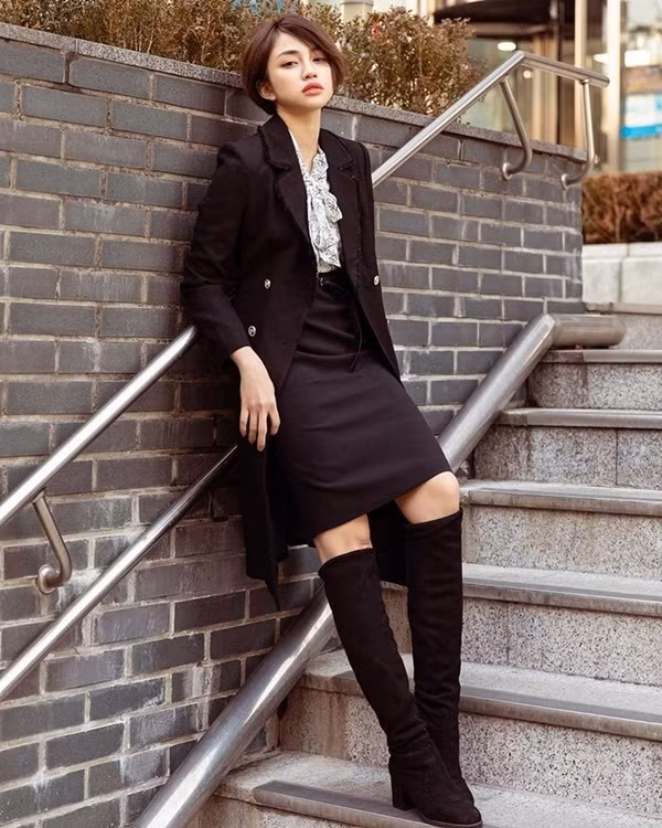 Thiên Nga lại chọn kết hợp sơ mi buộc nơ cùng áo khoác dáng dài, chân váy và boots tối màu. Bộ cánh thu đông với hai tông màu chủ đạo đen trắng mang đến cho cô vẻ ngoài sang chảnh, thời thượng nhưng không kém phần cá tính.