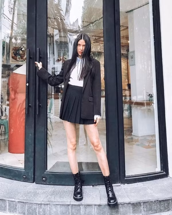 Để hoàn thiện set đồ theo phong cách preppy, Thùy Dương mix sơ mi trắng kết hợp cùng chân váy đen và blazer tiệp màu. Để nâng tầm set đồ cá tính này, cô nàng sử dụng đôi boots quân đội “chất lừ”.