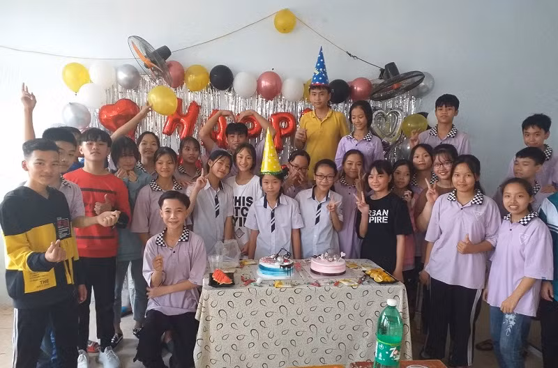 Nguyễn Thị Thúy Hà (giơ 2 ngón tay sau bạn nam cạnh bàn) vui vẻ cùng các bạn trong buổi sinh nhật tổ chức tại lớp.