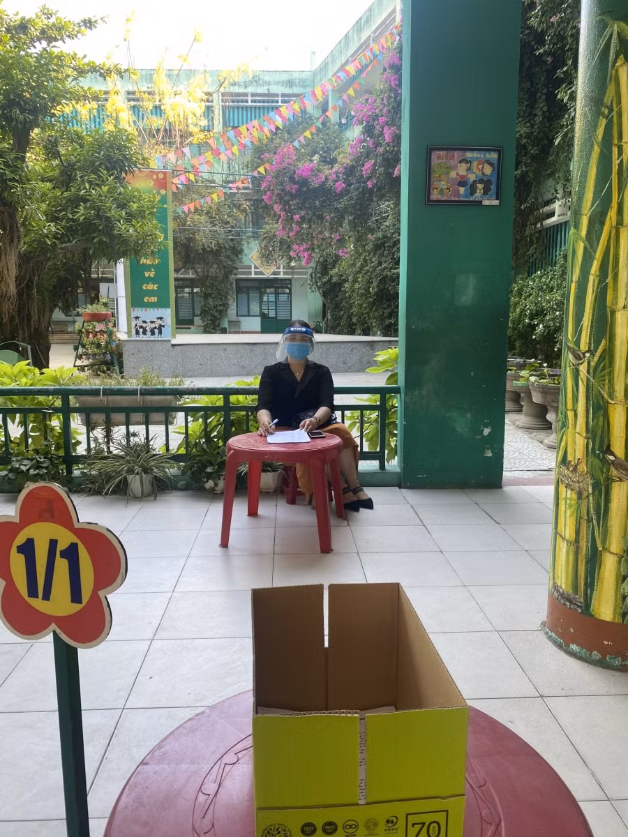 Giáo viên Trường Tiểu học Núi Thành (quận Hải Châu) sử dụng mũ ngăn giọt bắn dù đã thực hiện giãn cách khi giao nhận bài kiểm tra