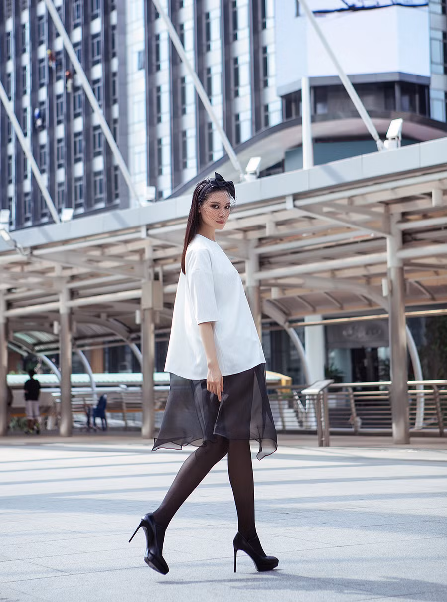 Váy suông tông trắng kết hợp cùng lớp voan mỏng nhẹ nhàng, bay bổng. Tất đen phối ăn ý cùng giày cao gót, nơ cài tóc đồng màu.