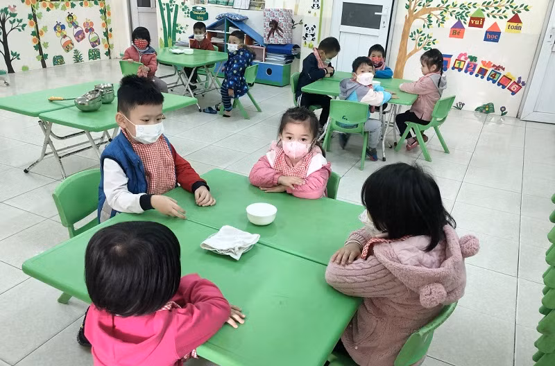 Trẻ ngồi theo khoảng cách để chuẩn bị vào giờ ăn trưa tại Trường Mầm non Lương Khánh Thiện.