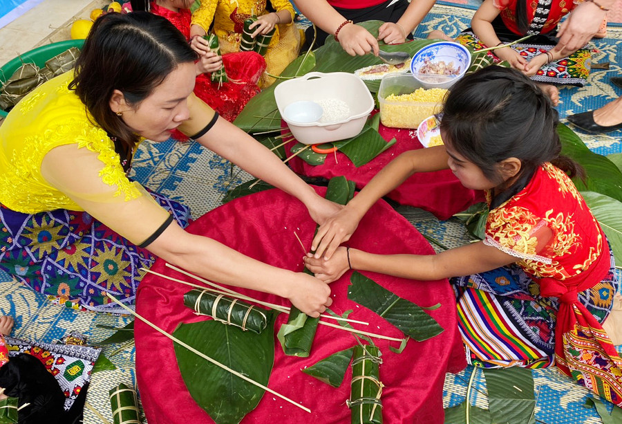 Cô giáo hướng dẫn học sinh tự tay gói bánh chưng trong hoạt động trải nghiệm Ngày Tết quê em.