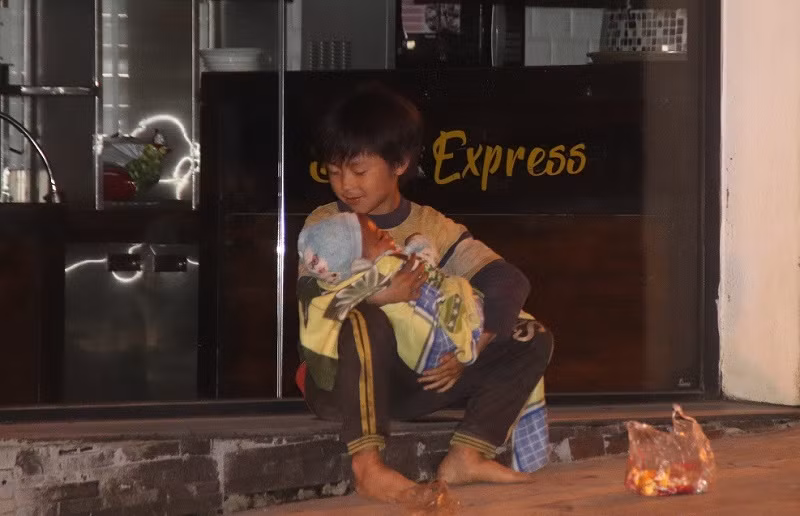 Một bé trai đang ôm em nhỏ ngủ gật gù trên tay lúc 23 giờ trên đường Cầu Mây, thị xã Sa Pa.