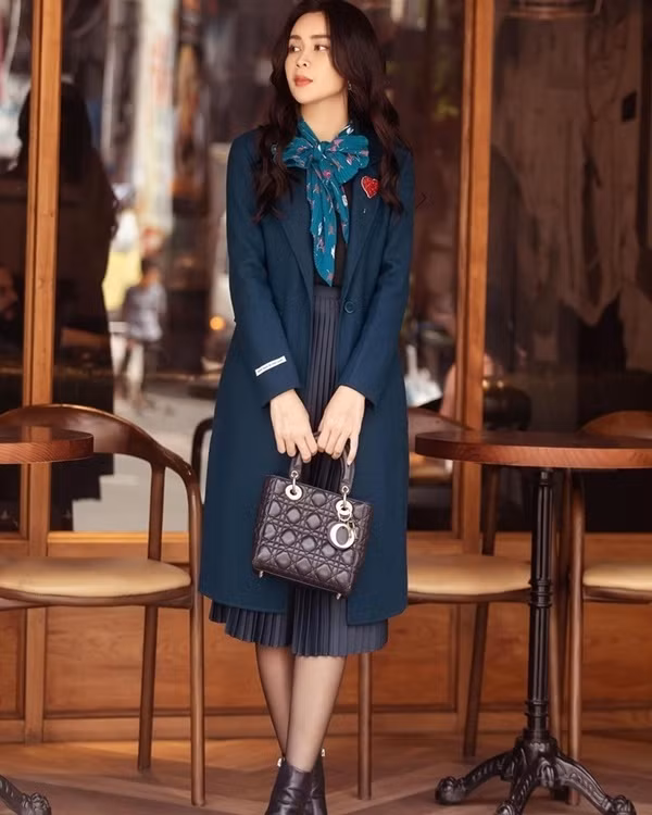 Ghép đôi chân váy xếp ly và áo len, Lưu Hương Giang làm bật vẻ thời thượng sang chảnh cho diện mạo bằng áo khoác dáng dài thắt nơ khăn ở cổ.
