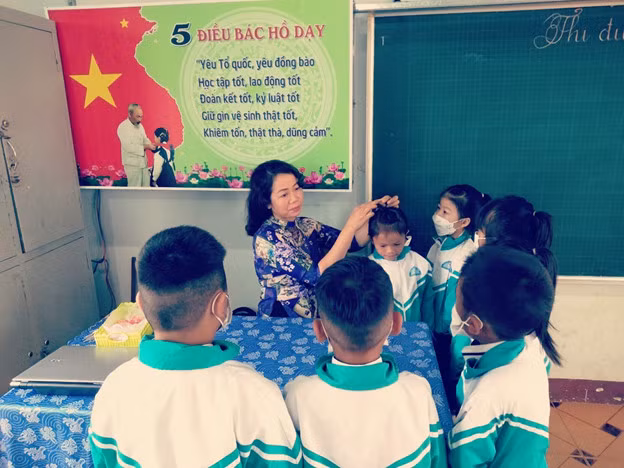 Giáo viên Trường Tiểu học Lê Lợi, buôn M’Hăng, xã Cư Huê, huyện EaKar (Đắk Lắk) hướng dẫn học sinh buộc tóc. Ảnh: NTCC