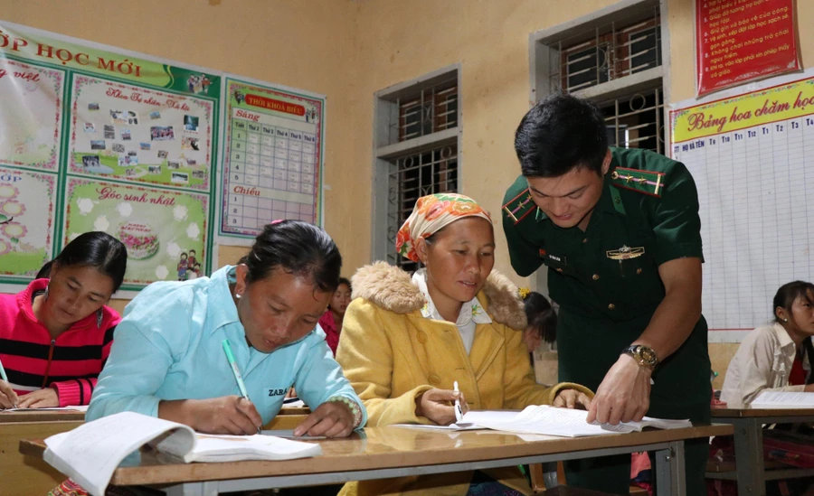 Thầy giáo Vì Văn Liêm, Đồn biên phòng Mường Lạn đang chỉ dẫn người dân đọc và viết chữ.