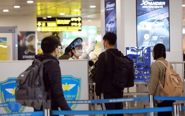 Nhân viên an ninh hàng không tại sân bay Nội Bài kiểm tra thân nhiệt của hành khách. (Ảnh: Huy Hùng/TTXVN).