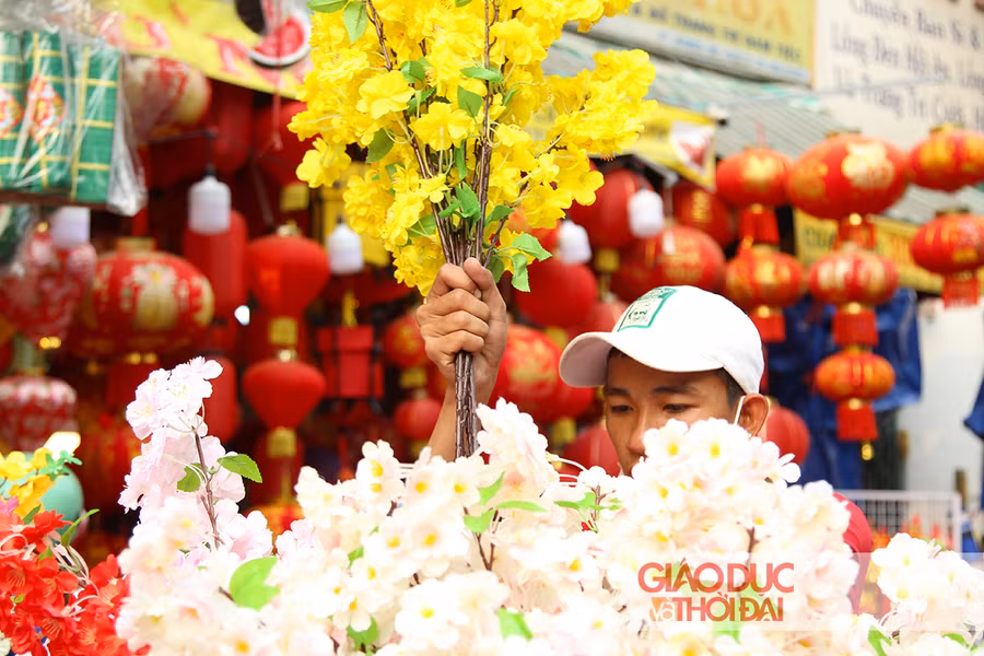 Từng cành hoa mai, hoa đào bằng vải được người bán sắp xếp xen kẽ, khoe sắc khắp một đoạn đường dài.