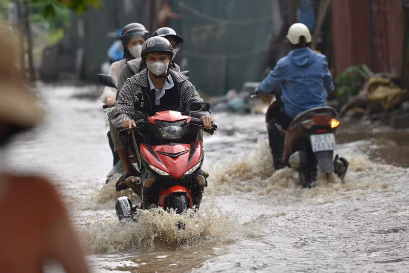 Người dân Hà Nội co chân trên xe máy lội qua đường ngập dù trời không mưa