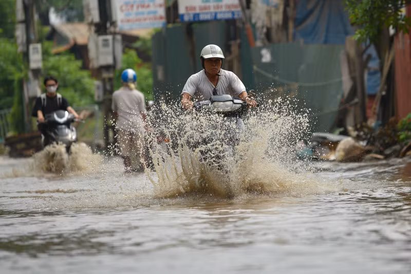 Người dân Hà Nội co chân trên xe máy lội qua đường ngập dù trời không mưa