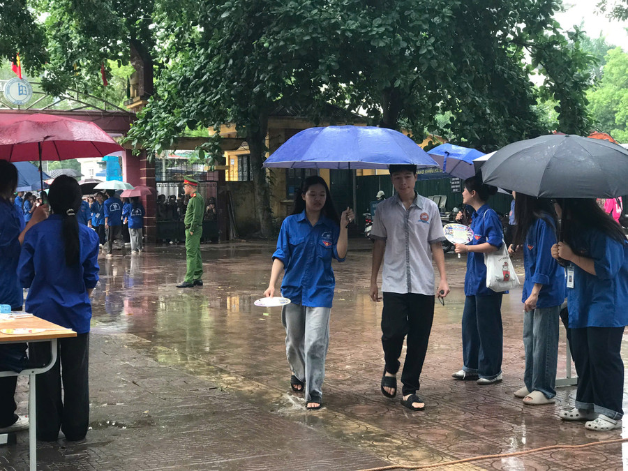 Thanh niên tình nguyện "đội mưa" hỗ trợ thí sinh vào khu vực phòng thi.
