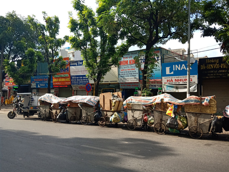 Hàng dài xe rác trên đường Hoàng Quốc Việt được công nhân vệ sinh phủ bạt chờ vận chuyển.