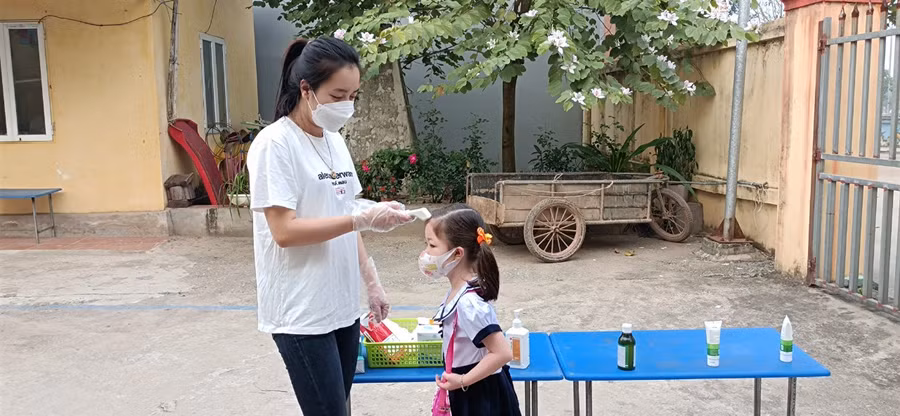 Giáo viên đo thân nhiệt cho trẻ từ cổng trường.