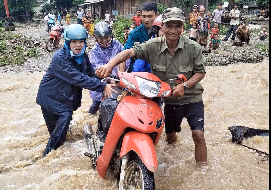 Bà con giúp cô giáo đẩy xe qua đoạn suối nước chảy xiết để vào trường. Ảnh: Đ. Thọ