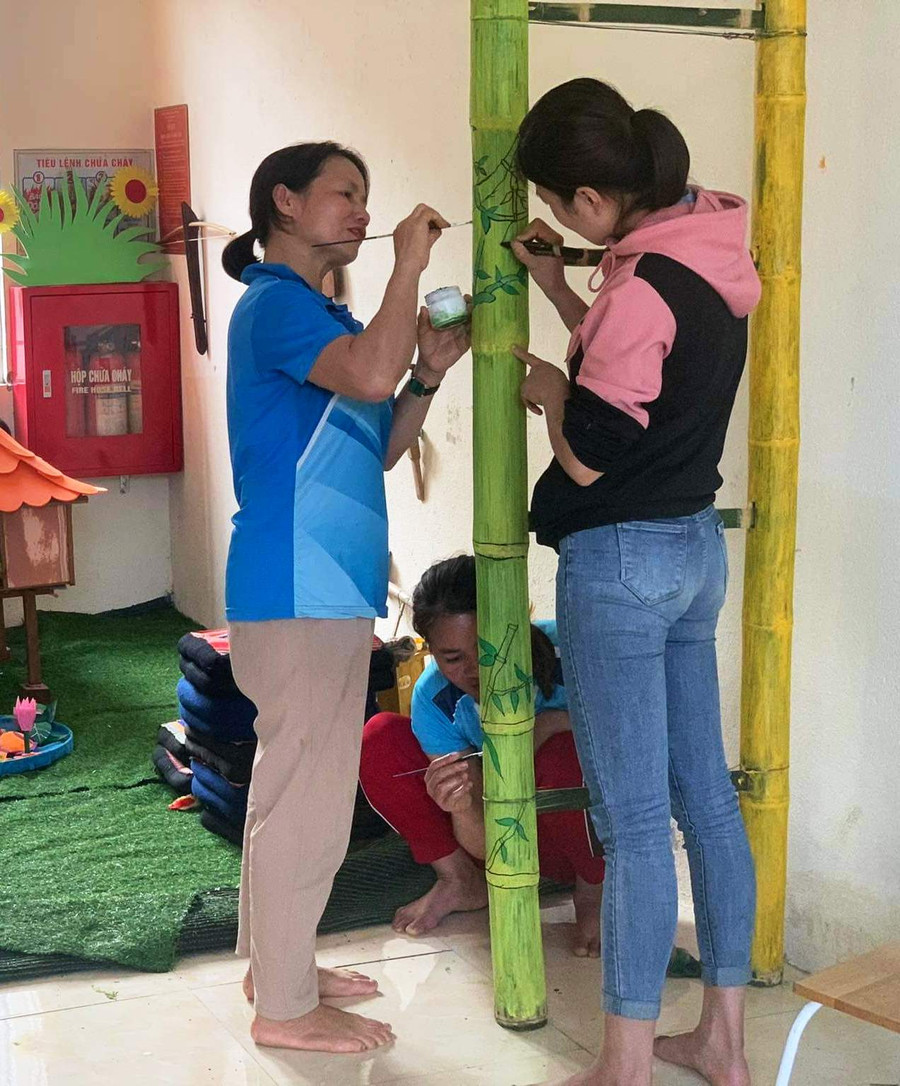 Các cô giáo đang vẽ hoa trên cột luồng. Ảnh: TL.