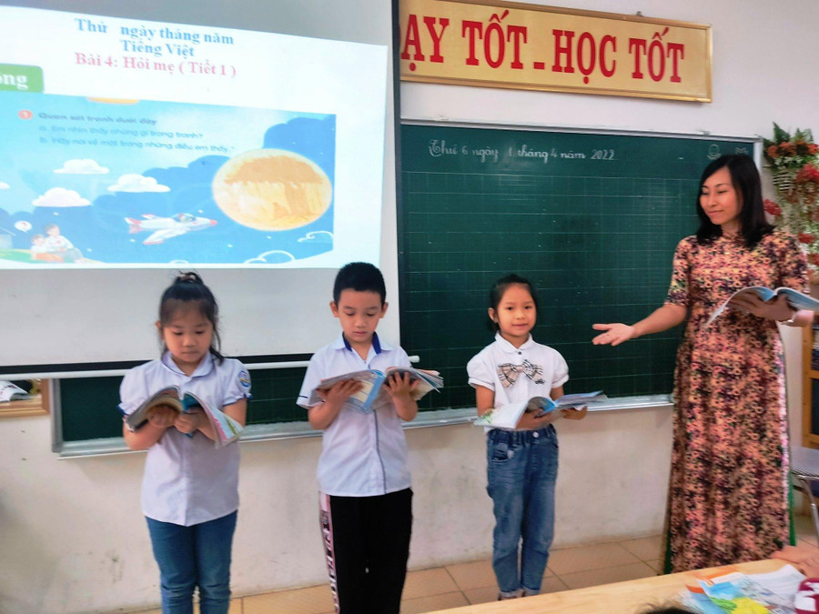 Cô giáo Hà hướng dẫn học sinh cách cầm sách đứng đọc. Cô giáo Hà hướng dẫn học sinh cách cầm sách đứng đọc.