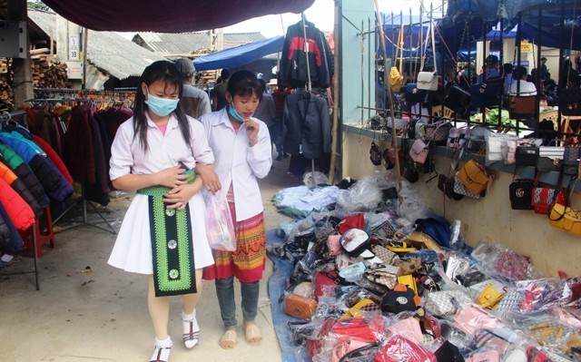 Hai thiếu nữ dân tộc Mông đi tìm những món hàng cần mua trong chợ phiên.