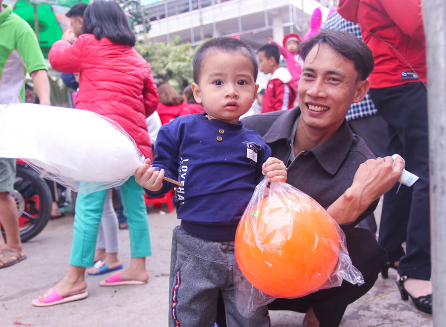 Anh Vũ Văn Đại (xã Quỳnh Hưng, huyện Quỳnh Lưu, Nghệ An) đưa con đi chợ tết. Anh cho biết, vợ anh đang đưa cháu lớn đi mua sắm quần áo, còn anh bế cháu thứ 2 đi dạo quanh chợ. Cháu bé có được quả bóng và cây kẹo bông nên không đòi gì nữa