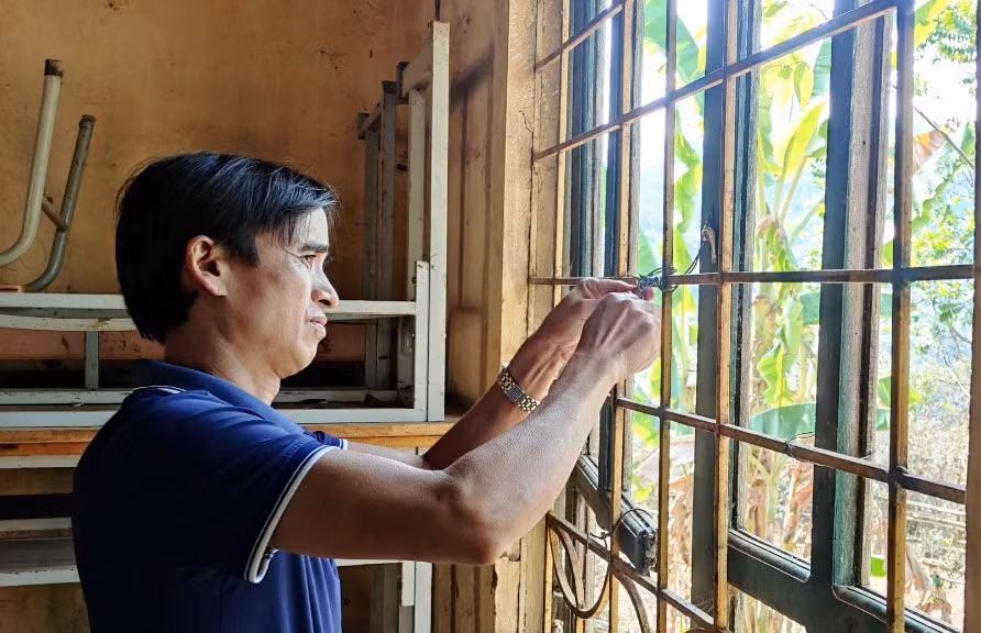 Thầy Hà Văn Chiềng đang buộc lại những thanh cửa sổ của phòng học. Ảnh: Thế Lượng.