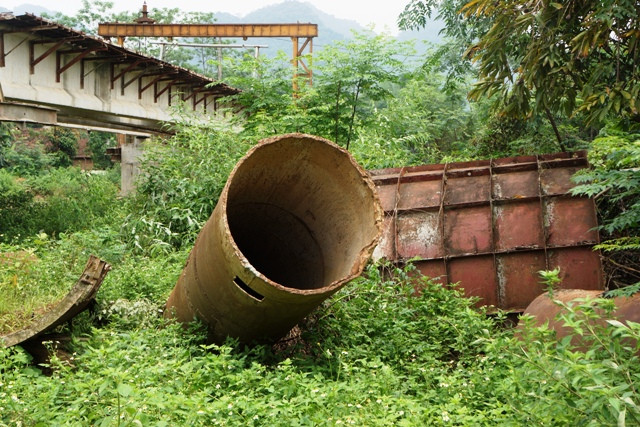 Nhiều thiết bị phục vụ thi công ngổn ngang dưới gầm cầu, cây cỏ mọc um tùm.