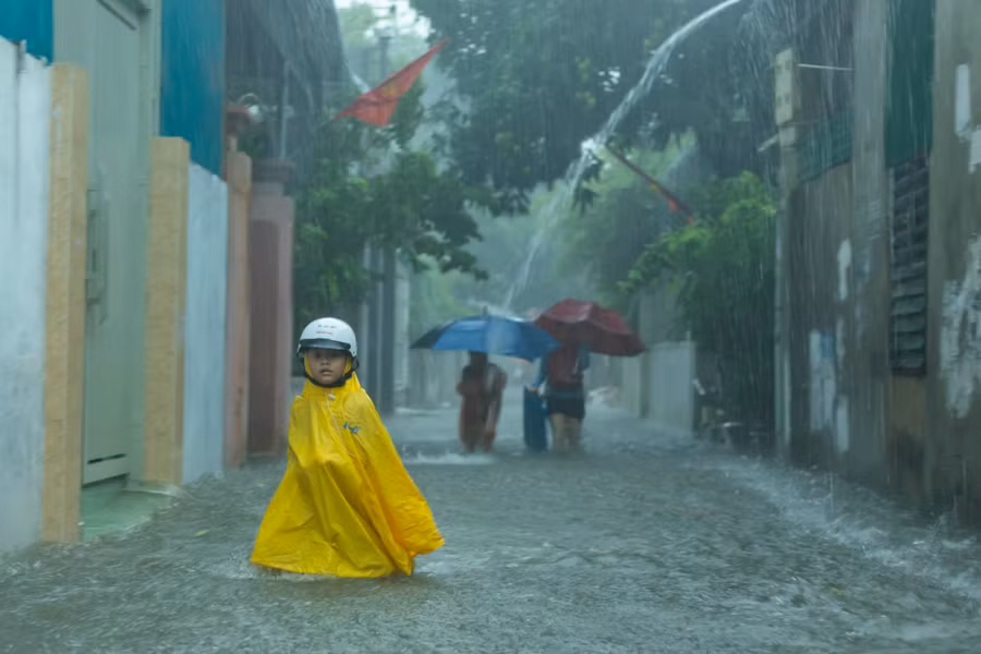Một em học sinh đội áo mưa đi bộ về nhà do ngõ phố ngập sâu, xe không lưu thông được.