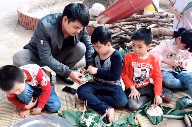 Phụ huynh học sinh đến trường chỉ dạy cho con cách gói bánh chưng ngày Tết.