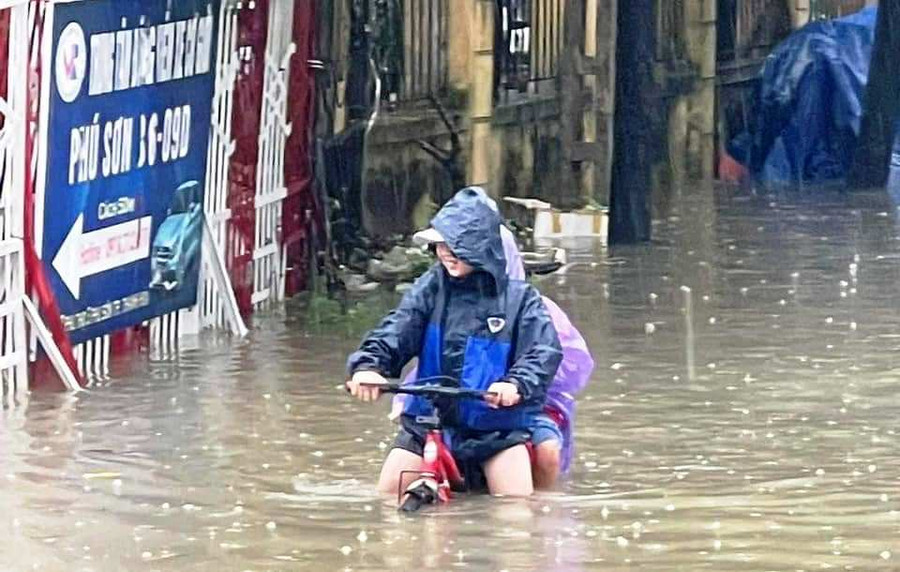 Hai nam sinh chở nhau đến trường giữa lúc trời mưa to, nước ngập sâu. (Ảnh: Bạn đọc cung cấp)