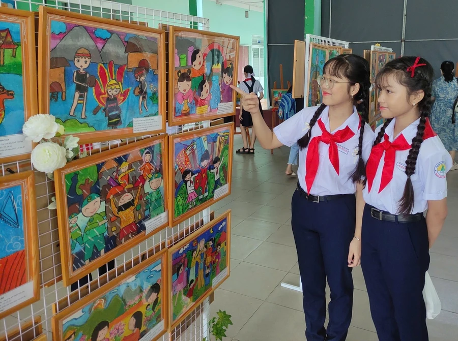 Hai em học sinh đang ngắm các bức vẽ của các thí sinh tham gia hội thi vẽ tranh "Em vẽ sắc màu quê hương". Ảnh: Nhà thiếu nhi Bình Dương