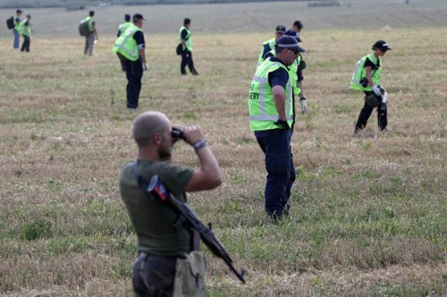 Các điều tra viên làm việc khi một phiến quân ở đông Ukraine theo dõi bằng ống nhòm. Ảnh: Reuters