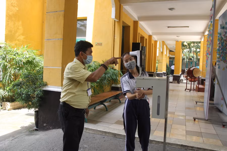 Cán bộ tại điểm thi Trường THPT Trưng Vương hướng dẫn thí sinh đo thân nhiệt trước khi vào phòng thi.