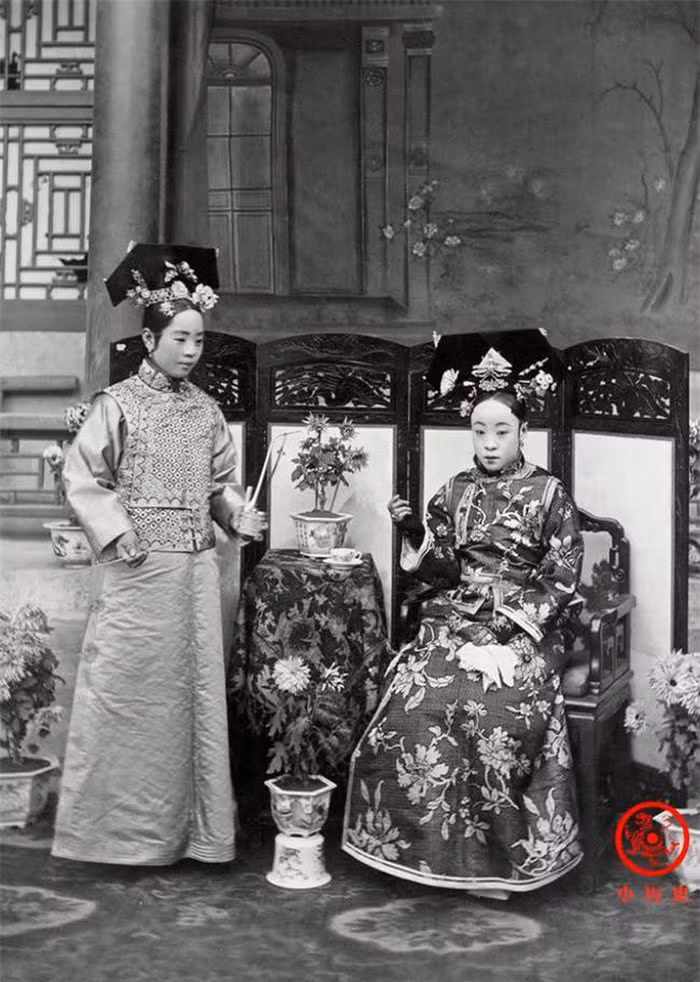 Người đang ngồi là mẹ ruột của Hoàng đế Phổ Nghi, vị Hoàng đế cuối cùng của nhà Thanh và cũng là Hoàng đế cuối cùng của chế độ phong kiến Trung Hoa. Cô gái bên trái là gia nhân của bà, đang hầu hạ bà uống trà.