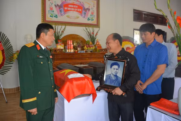 Đại tá Dư Công Thịnh (bên trái) bàn giao hài cốt liệt sĩ Hà Công Thiên cho gia đình; ông Hà Công Lực ôm di ảnh người thân.