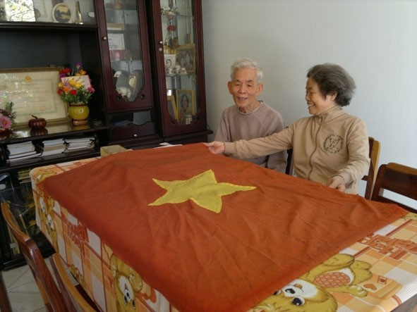Bà Nguyễn Thị Ngọc Lan cùng chồng - ông Nguyễn Du (lúc còn sống) bên kỷ vật là lá cờ Tổ quốc do chính tay bà may. Ảnh: TT -HG