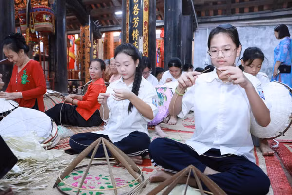 Các em học sinh được các nghệ nhân truyền nghề làm nón lá làng Chuông. Ảnh: Đình Tuệ.