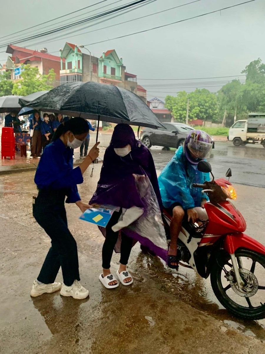 Tình nguyện viên Điểm thi trường THPT Tân Yên số 1 che mưa đón thí sinh vào khu vực phòng thi sáng 8/7.