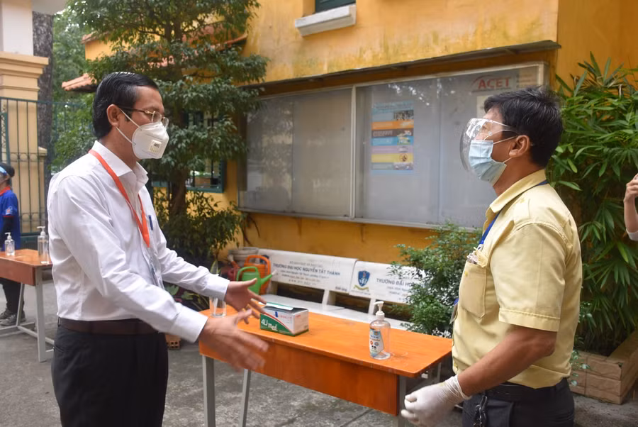 Thứ trưởng Nguyễn Văn Phúc (trái) hỏi thăm cán bộ phụ trách vệ sinh sát khuẩn tại điểm thi Trường THPT Trưng Vương.