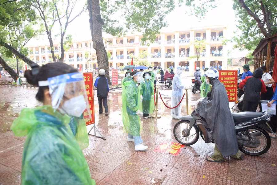 Lực lượng tình nguyện đeo khẩu trang, mũ chắn giọt bắn hướng dẫn thí sinh phòng dịch Covid-19.