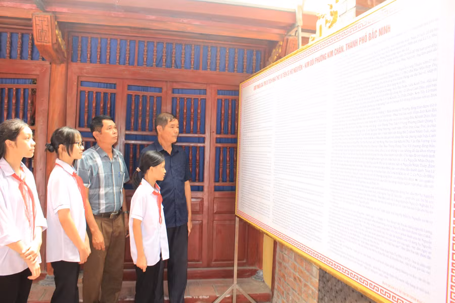 Ông Nguyễn Văn Điết và ông Nguyễn Văn Hùng cùng các cháu học sinh trước bảng vàng ghi danh của dòng họ.