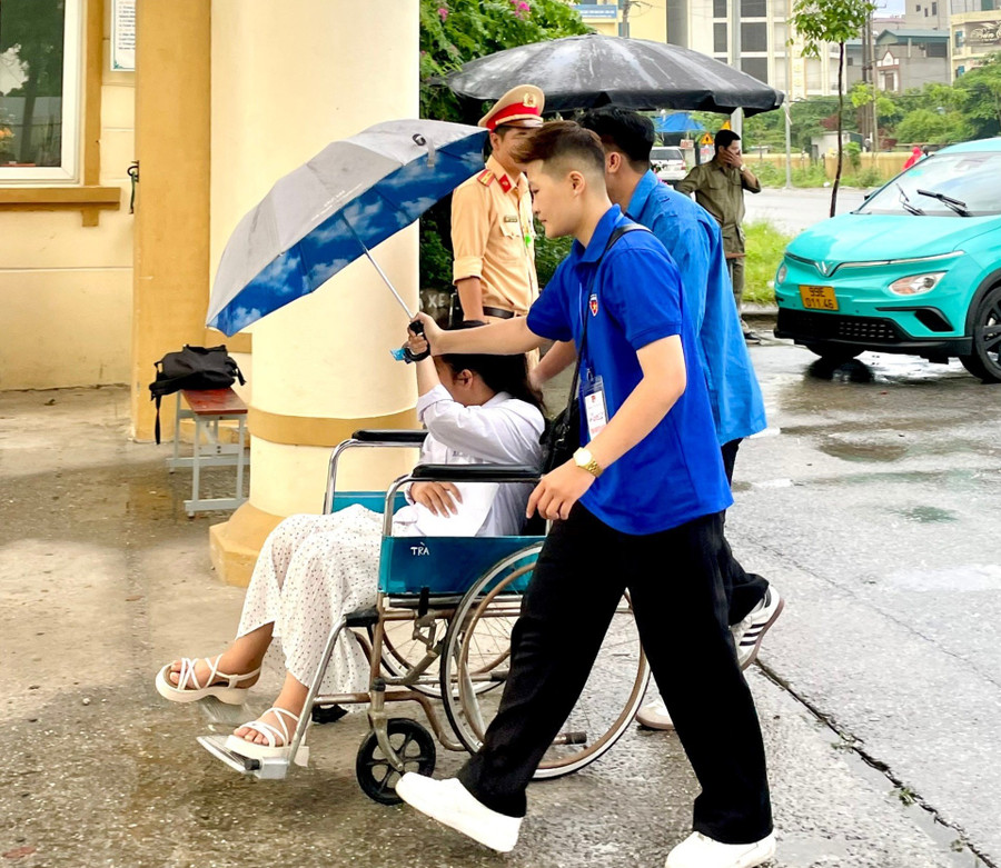 Thanh niên tình nguyện che ô, đẩy xe cho thí sinh không may bị gãy chân dự thi tại điểm thi Trường THPT Hàm Long (TP Bắc Ninh). Thanh niên tình nguyện che ô, đẩy xe cho thí sinh không may bị gãy chân dự thi tại điểm thi Trường THPT Hàm Long (TP Bắc Ninh).