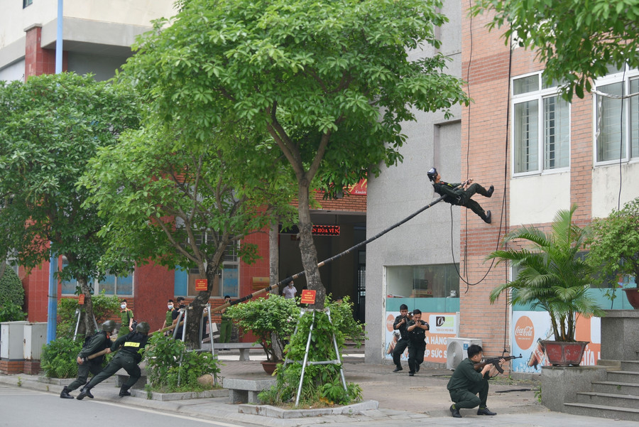 Tình huống giả định, mũi tấn công số 1 gồm các chiến sĩ tận dụng địa hình địa vật gồm nhiều cây cối và chướng ngại vật, thực hiện động tác lên sào trong chiến thuật đột nhập nhà cao tầng để áp sát toà nhà.