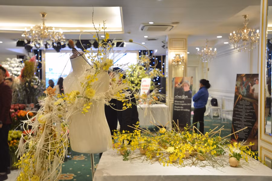 Tác phẩm của nhà thiết kế hoa Nhật Nguyễn. Nguyên liệu kết hợp giữa dây mây và gỗ, đan với nhau tạo thành hình dáng lạ mắt. Sau đó, hoàn thiện bằng hoa khô và hoa tươi có tông màu vàng chủ đạo.