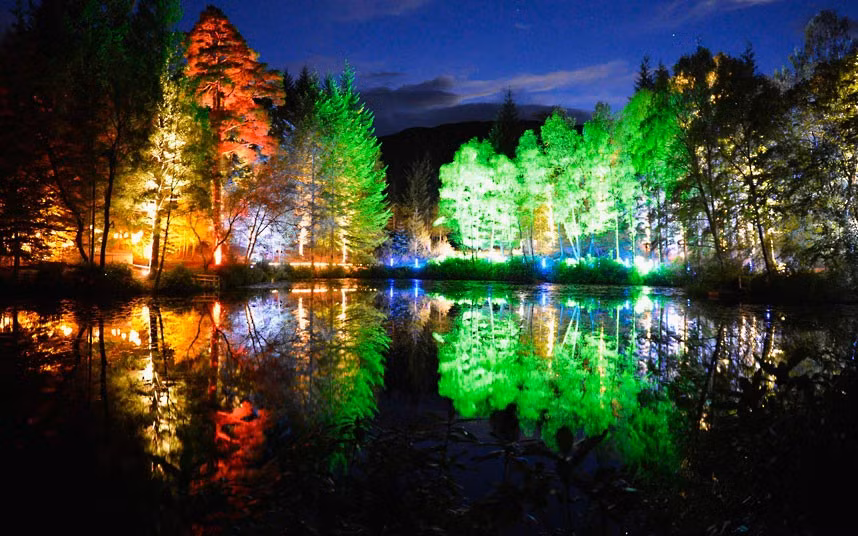 Trees lit by coloured lights are reflected in Loch Dunmore in Faskally Wood, in Pitlochry, Scotland