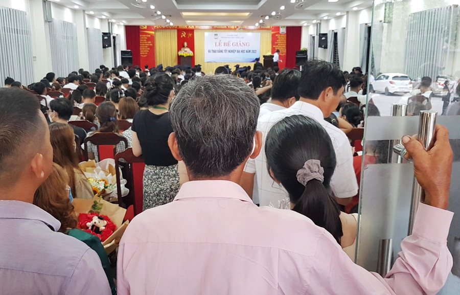 Một phụ huynh tóc đã điểm bạc đứng ngóng con từ góc cuối hội trường.