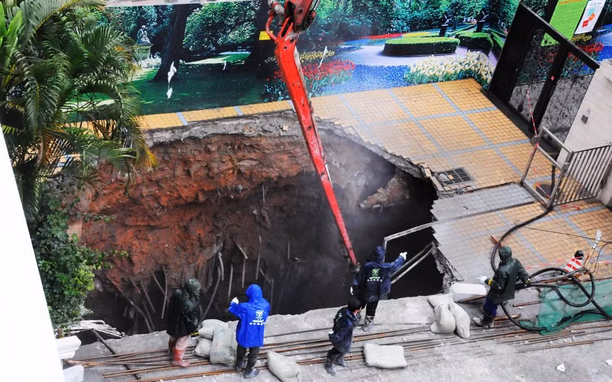 Workers examine a giant sink hole left in a street in Shenzhen, China. A security guard, who happened to walk past the area at the time of the collapse, fell into the hole and died.