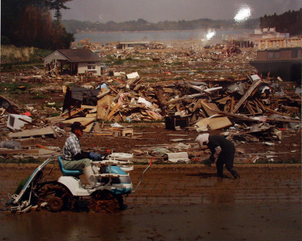 Từng bước tái xây dựng – Hai vợ chồng đang trồng lúa bên cạnh nơi vẫn còn ngổn ngang gạch đá đổ nát sau thảm họa ở thành phố Kesennuma, tỉnh Miyagi